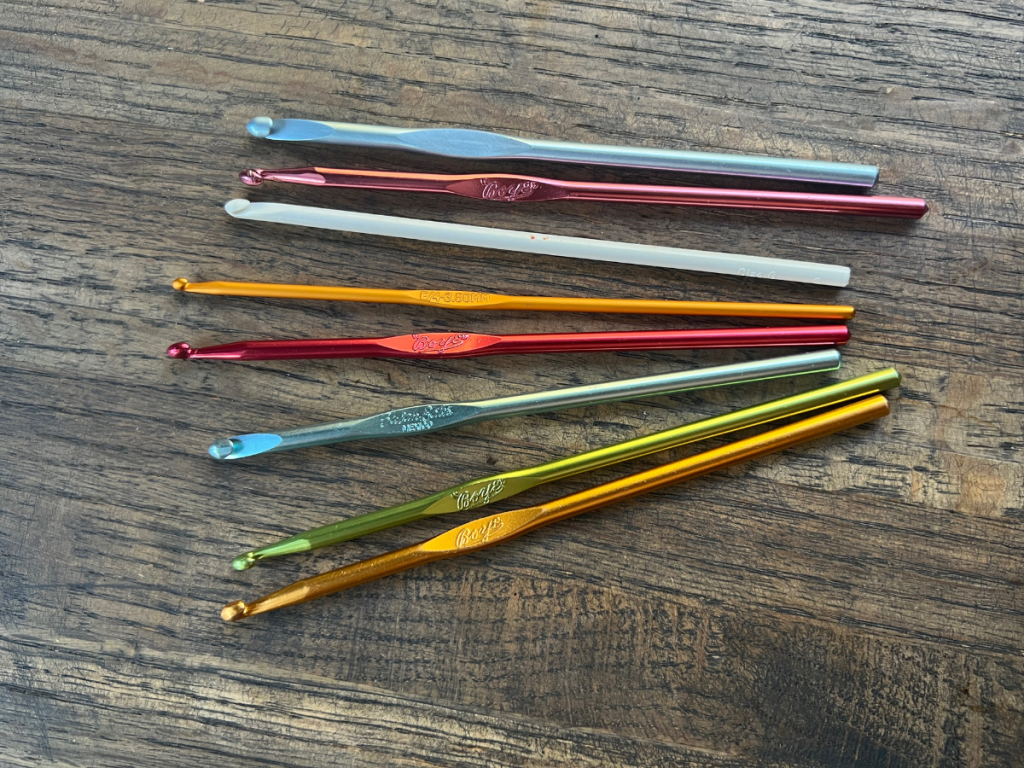 Different colored and type of crochet hooks laying on a wooden surface
