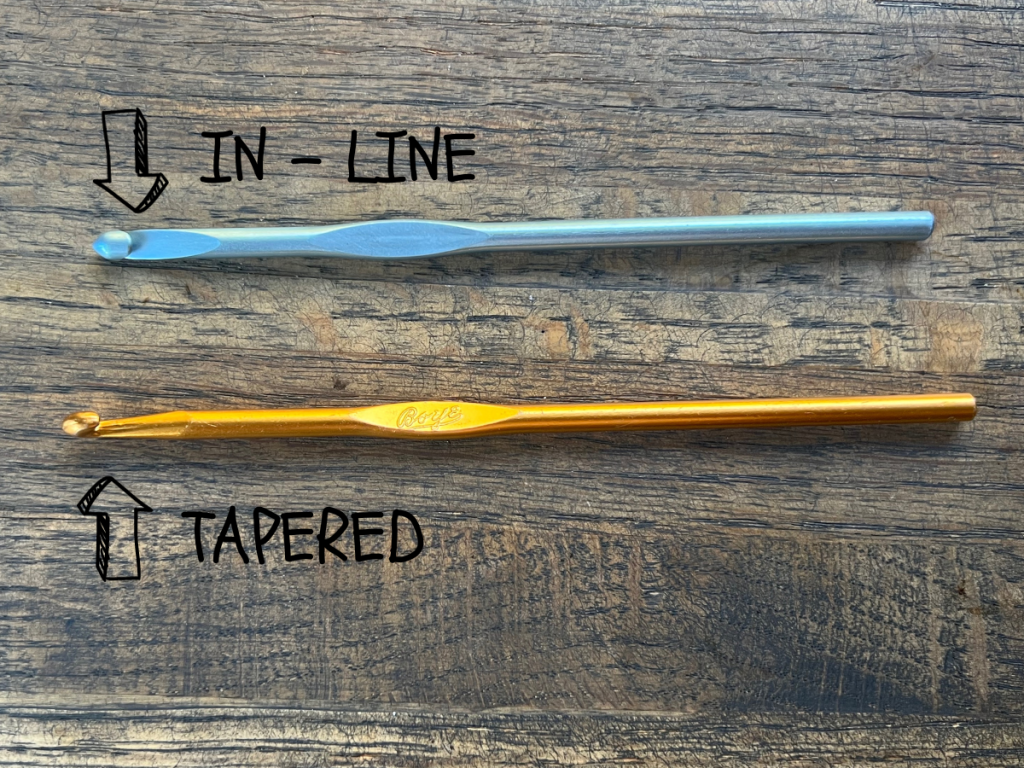 Blue in line crochet hook and gold tapered crochet hook laying on a wooden table