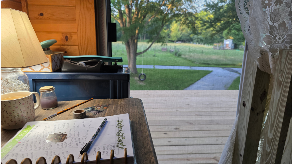 Open journal with pens, washi tape, watercolor brushes, and a view of a field